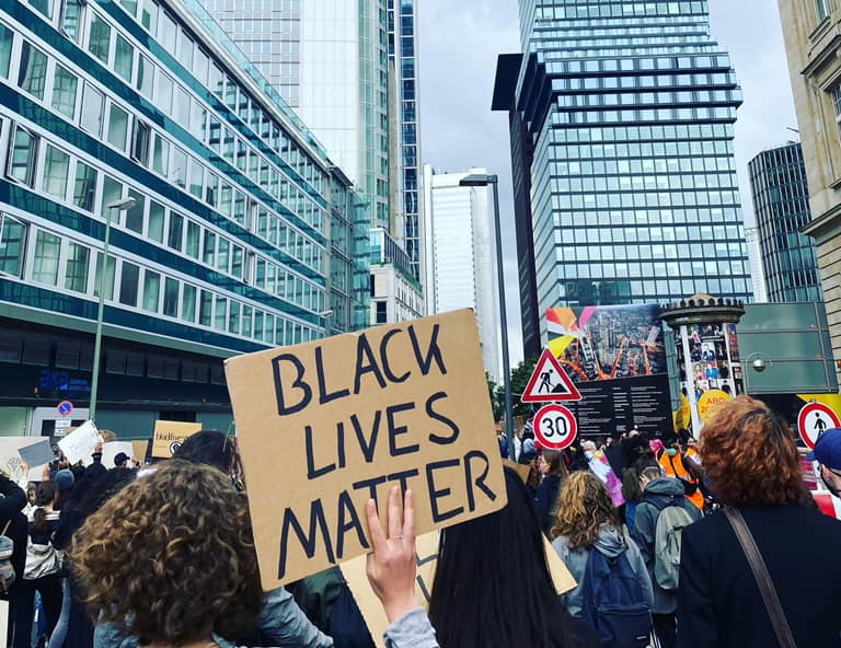 Demonstrantin hält Papptransparent hoch mit "Black Lives Matter"-Aufschrift zwischen den Frankfurter Bankentürme. Bild: M. Müller